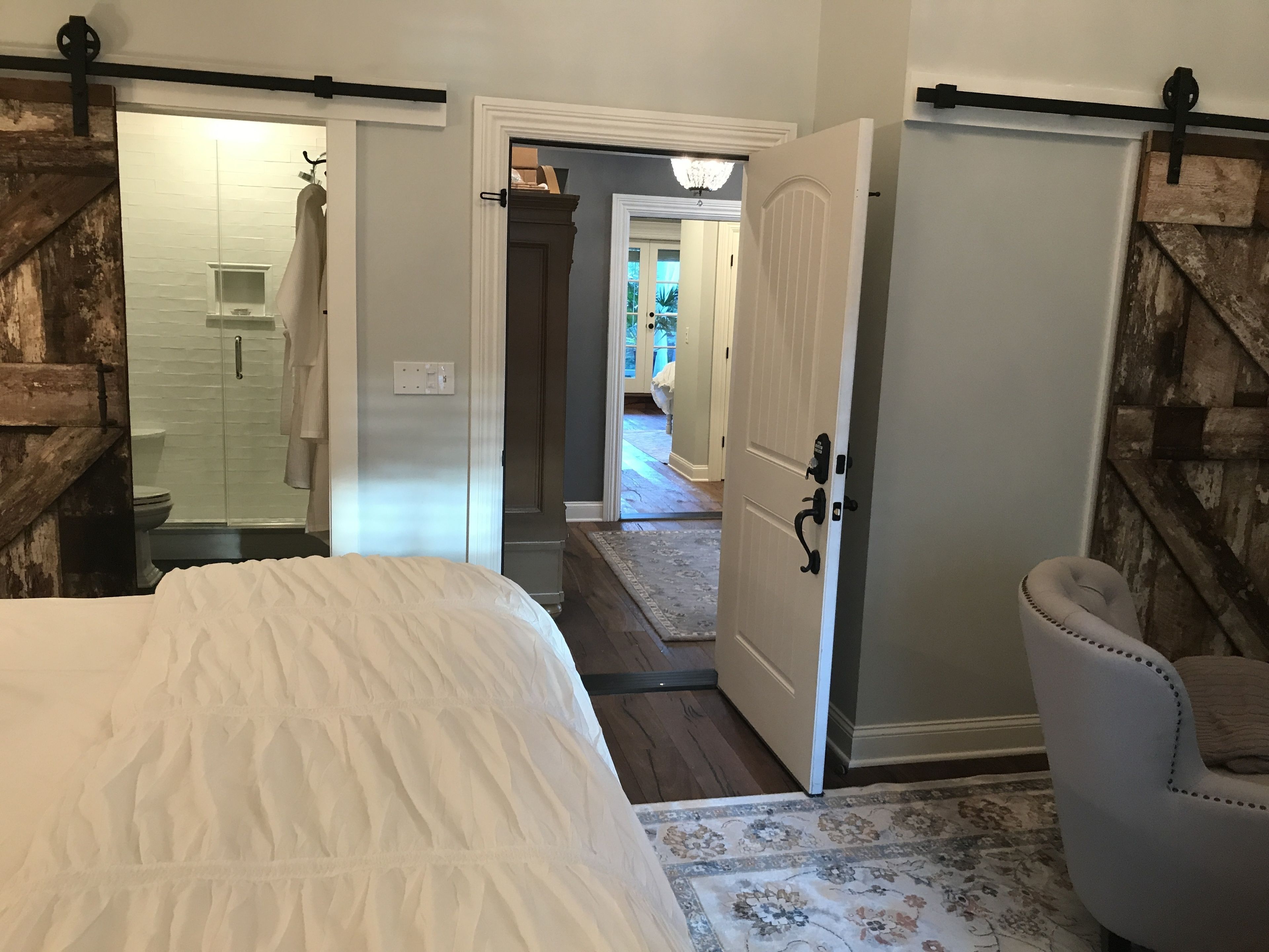 A bedroom with a large bed, a chair, a wardrobe, and a bathroom with a shower.