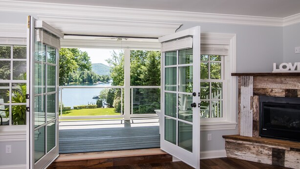 An open door leading to a deck with a view of a lake and greenery. - Chateau Rooms (Bolton Landing)