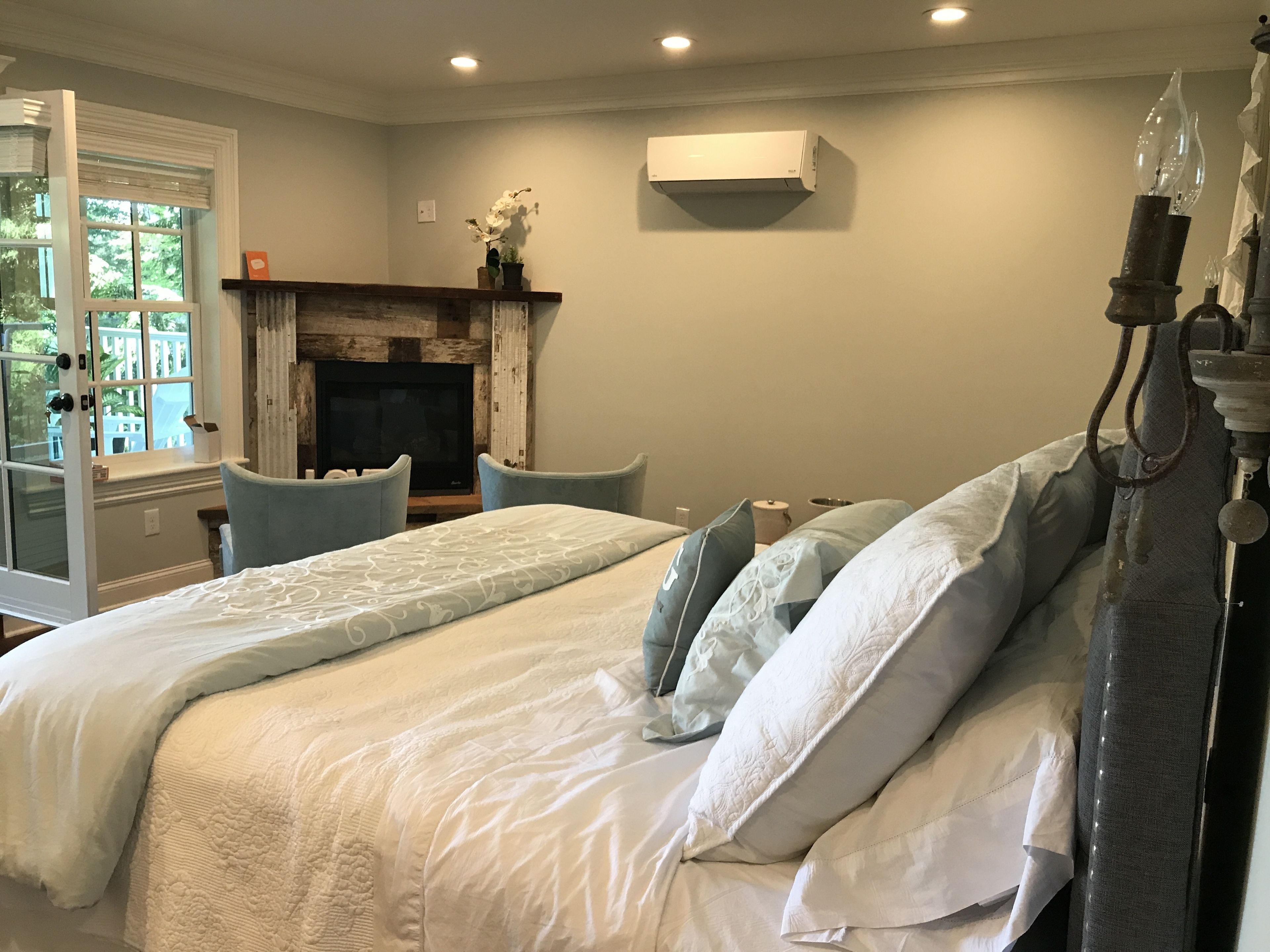 A bedroom with a bed, two chairs, a fireplace, and an air conditioning unit.