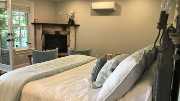 A bedroom with a bed, two chairs, a fireplace, and an air conditioning unit.