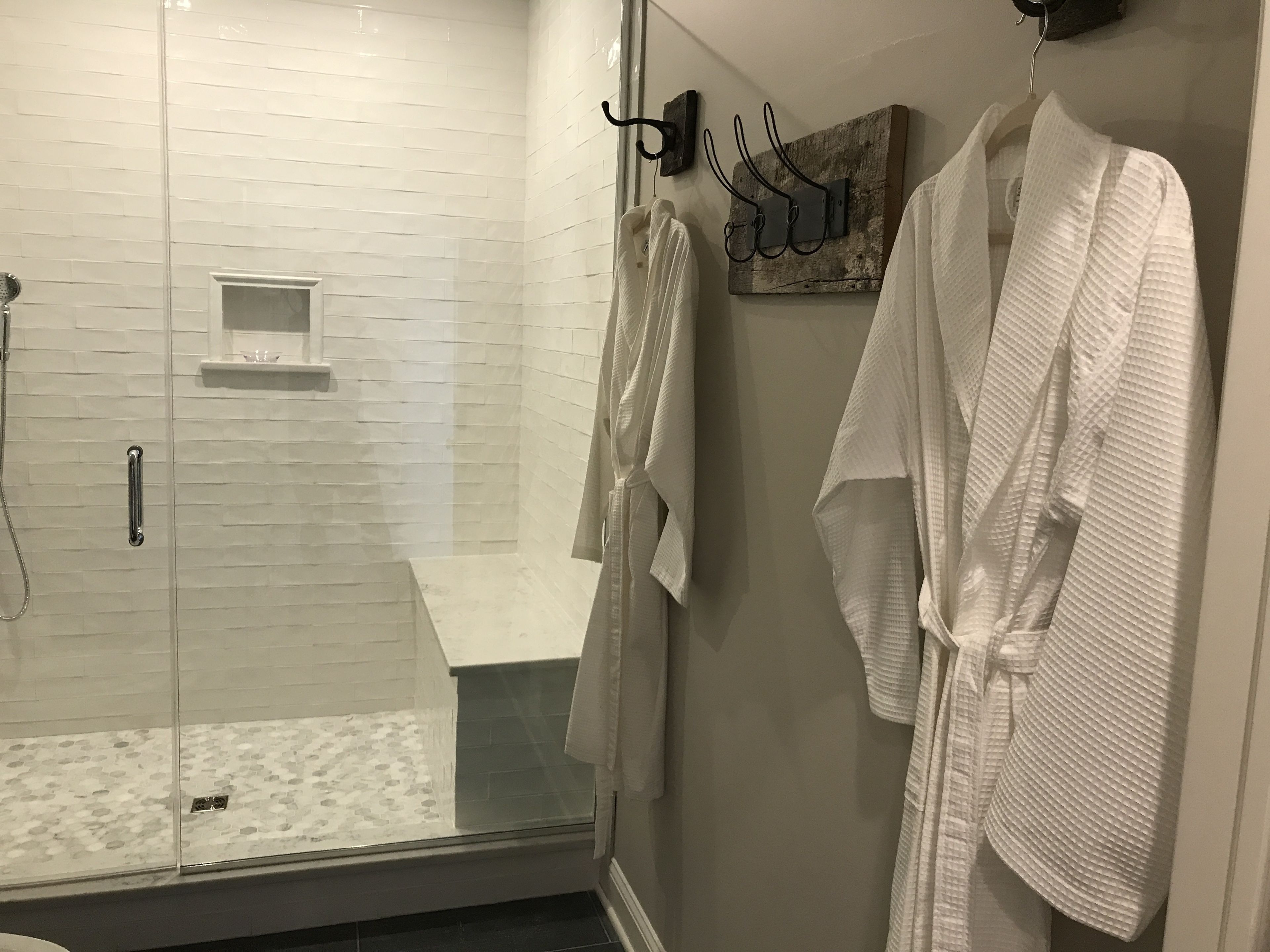 A modern bathroom with a glass-enclosed shower, white tiled walls, and a wooden bath mat.