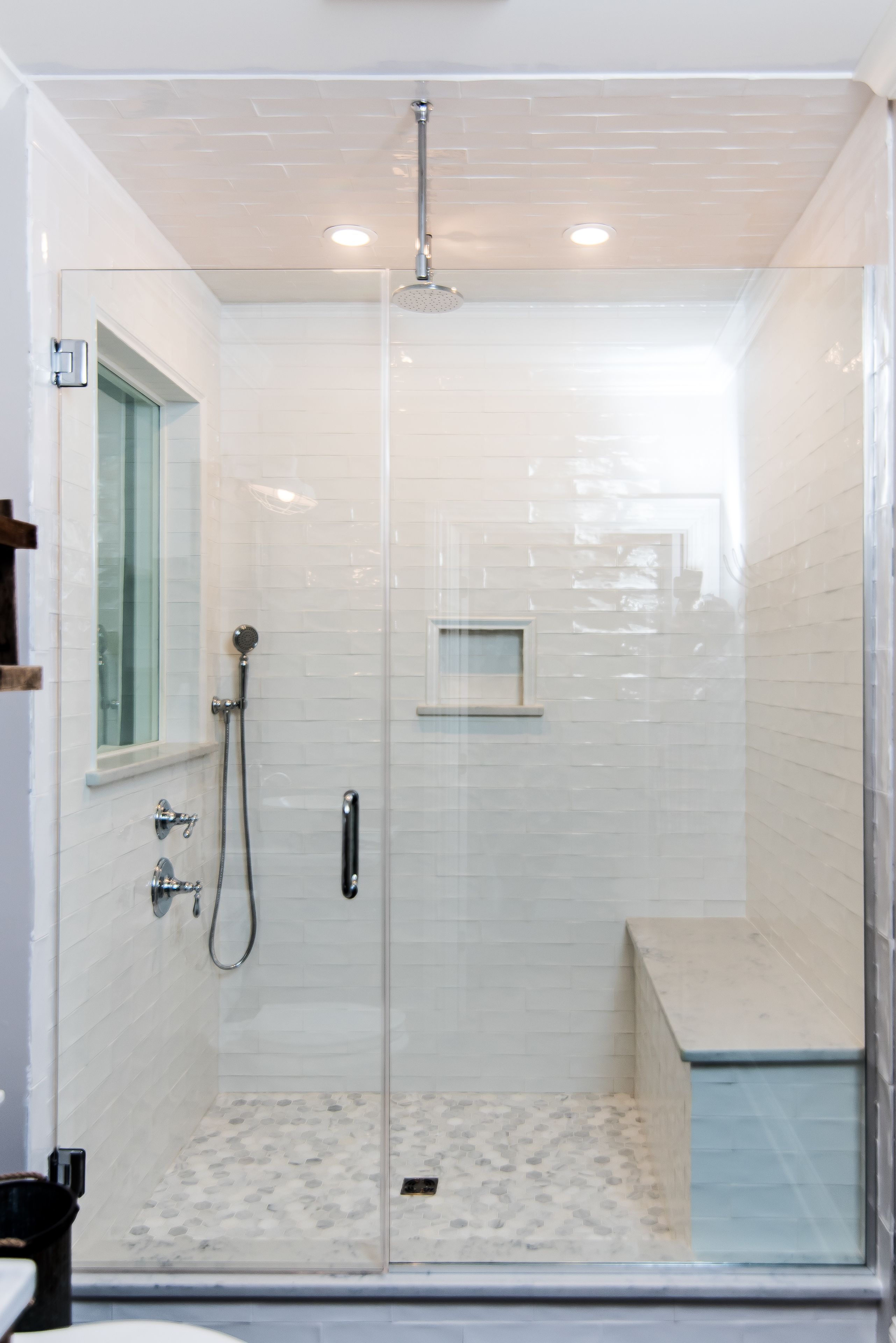 A glass-enclosed shower with a handheld showerhead, a small window, and a tiled floor.