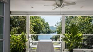 An outdoor patio with a table and chairs, surrounded by potted plants, overlooking a lake and forested area. - Chateau Rooms (Bolton Landing)