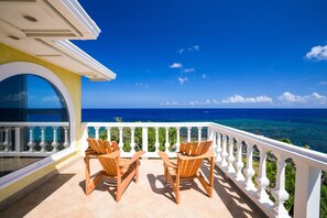 Ein Balkon mit zwei Holzstühlen mit Blick auf das klare, blaue Meer.