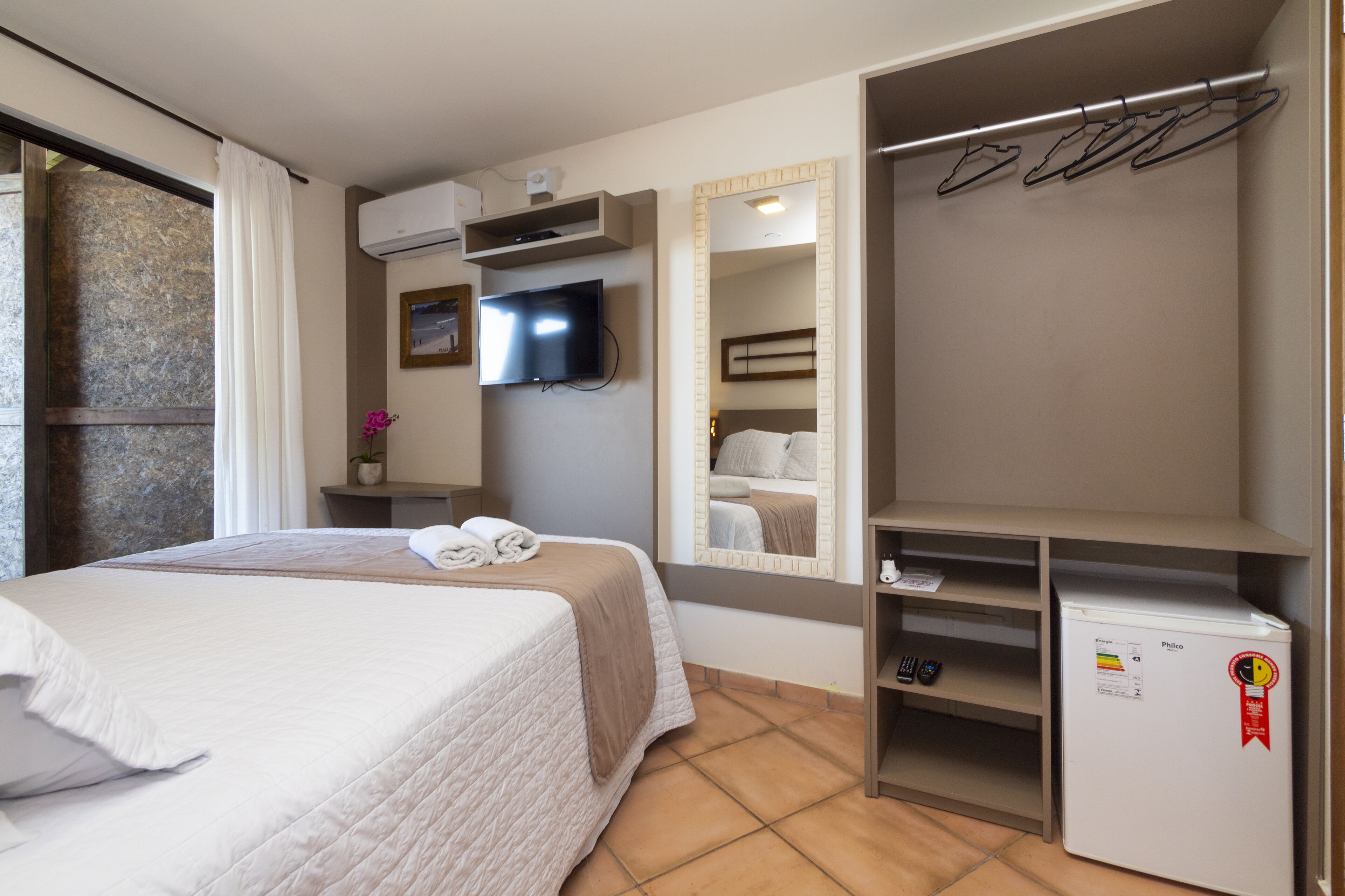 Une chambre d’hôtel équipée d’un lit, d’une télévision, d’un miroir, d’une armoire et d’un mini-réfrigérateur.
