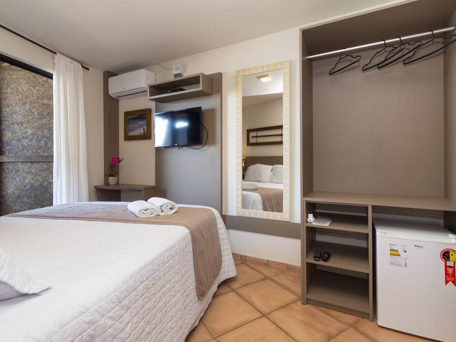 Une chambre d’hôtel équipée d’un lit, d’une télévision, d’un miroir, d’une armoire et d’un mini-réfrigérateur.