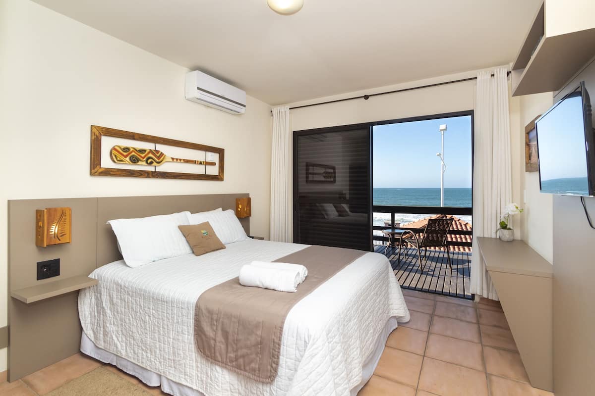 Habitación de hotel con cama, televisión, balcón con vistas al mar y ventilador de techo.