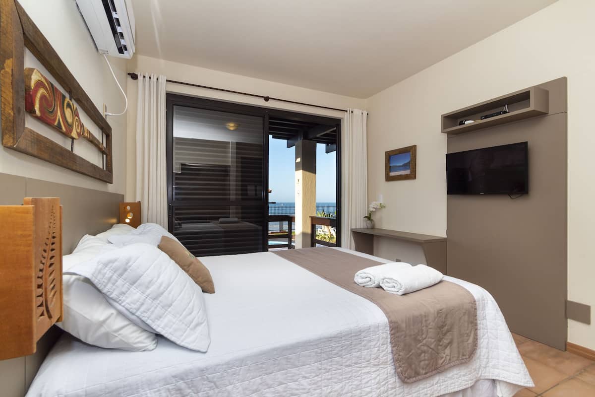 Una habitación de hotel con una cama grande, un televisor montado en la pared y un balcón con vistas.