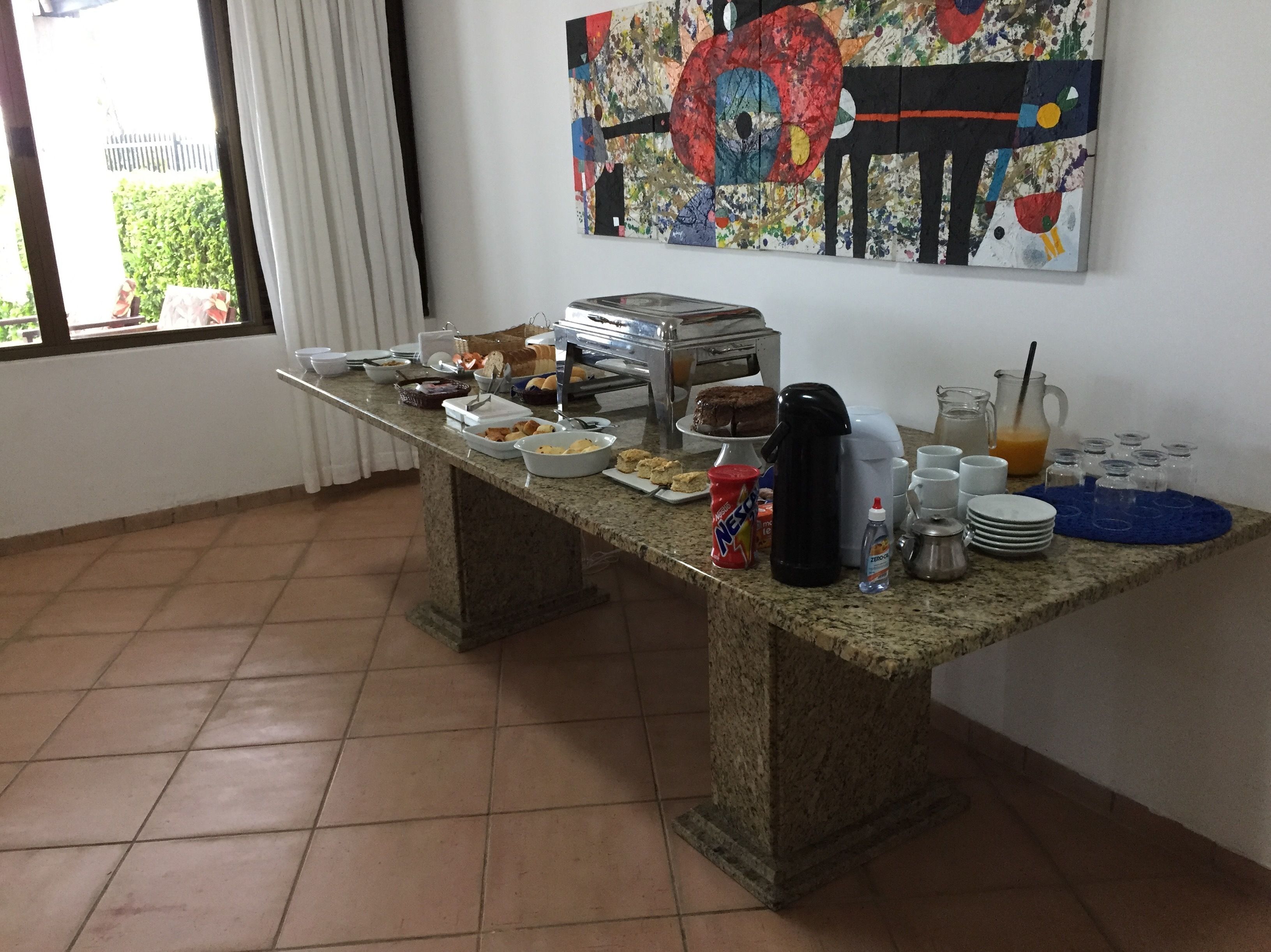 Un'impostazione per colazione a buffet con diversi cibi e bevande su un tavolo in granito, una macchina da caffè e un quadro appeso al muro.
