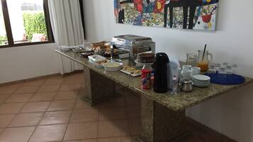Un'impostazione per colazione a buffet con diversi cibi e bevande su un tavolo in granito, una macchina da caffè e un quadro appeso al muro.
