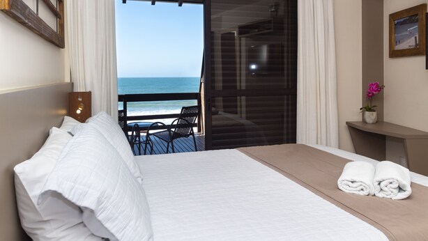 Habitación de hotel con cama, una mesita y una silla. Se ve el océano a través de un ventanal.