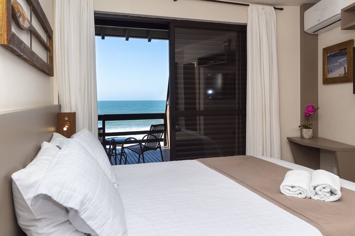 Habitación de hotel con cama, una mesita y una silla. Se ve el océano a través de un ventanal.
