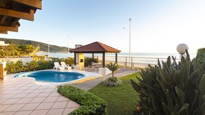 Una piscina con sillones de descanso, un pabellón y vista al mar.