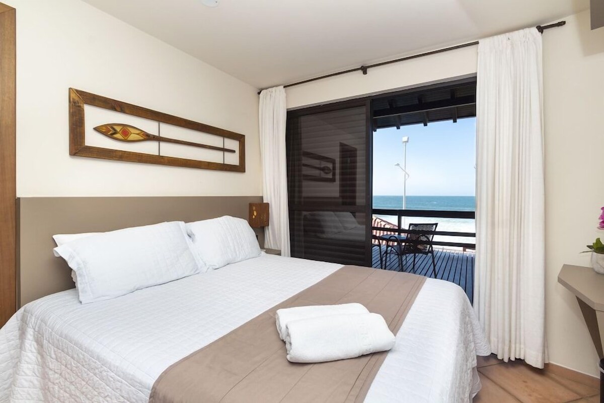 Une chambre d’hôtel avec un lit, une vue sur la mer et un balcon équipé d’une chaise.