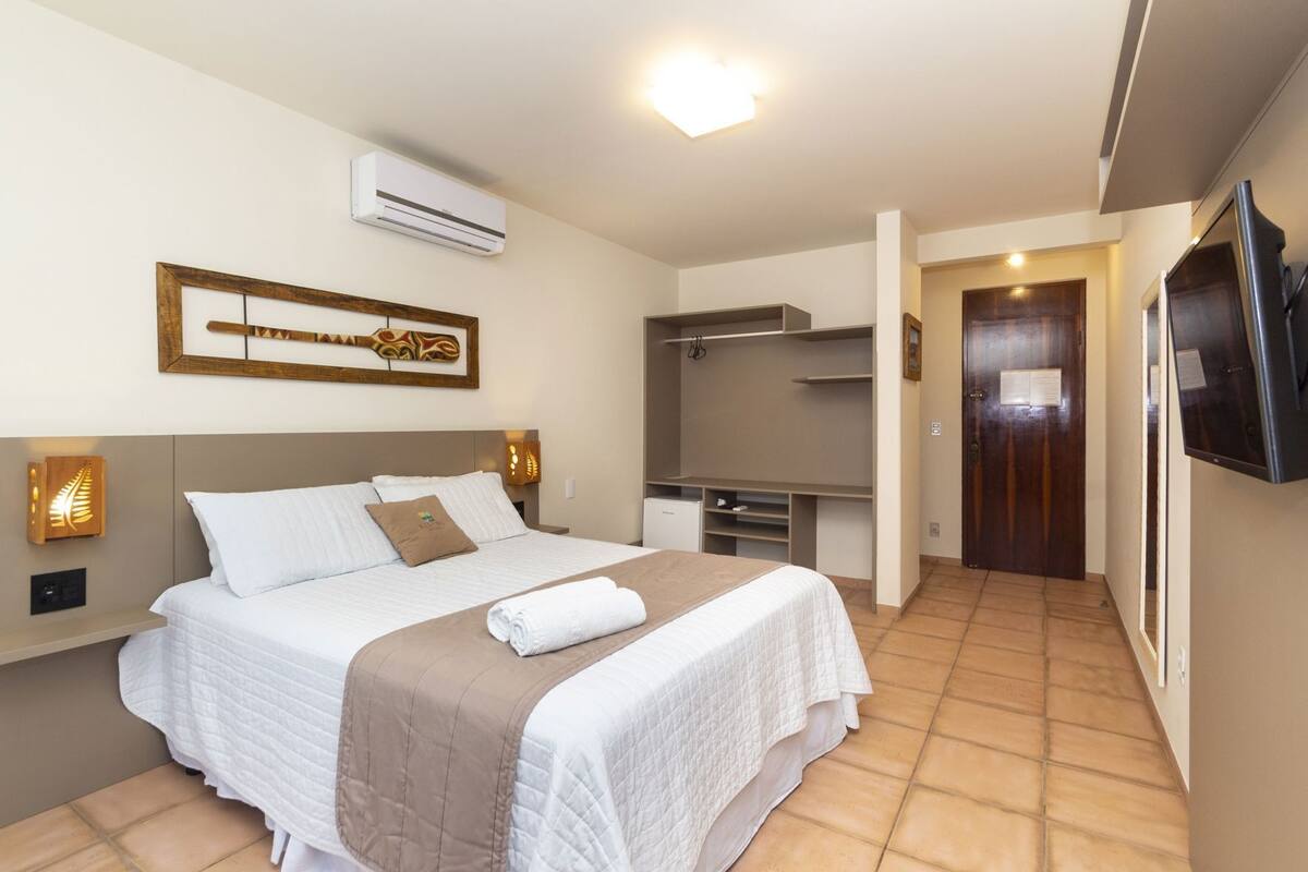 Un dormitorio con cama, mesitas de noche, aire acondicionado, armario y televisor.