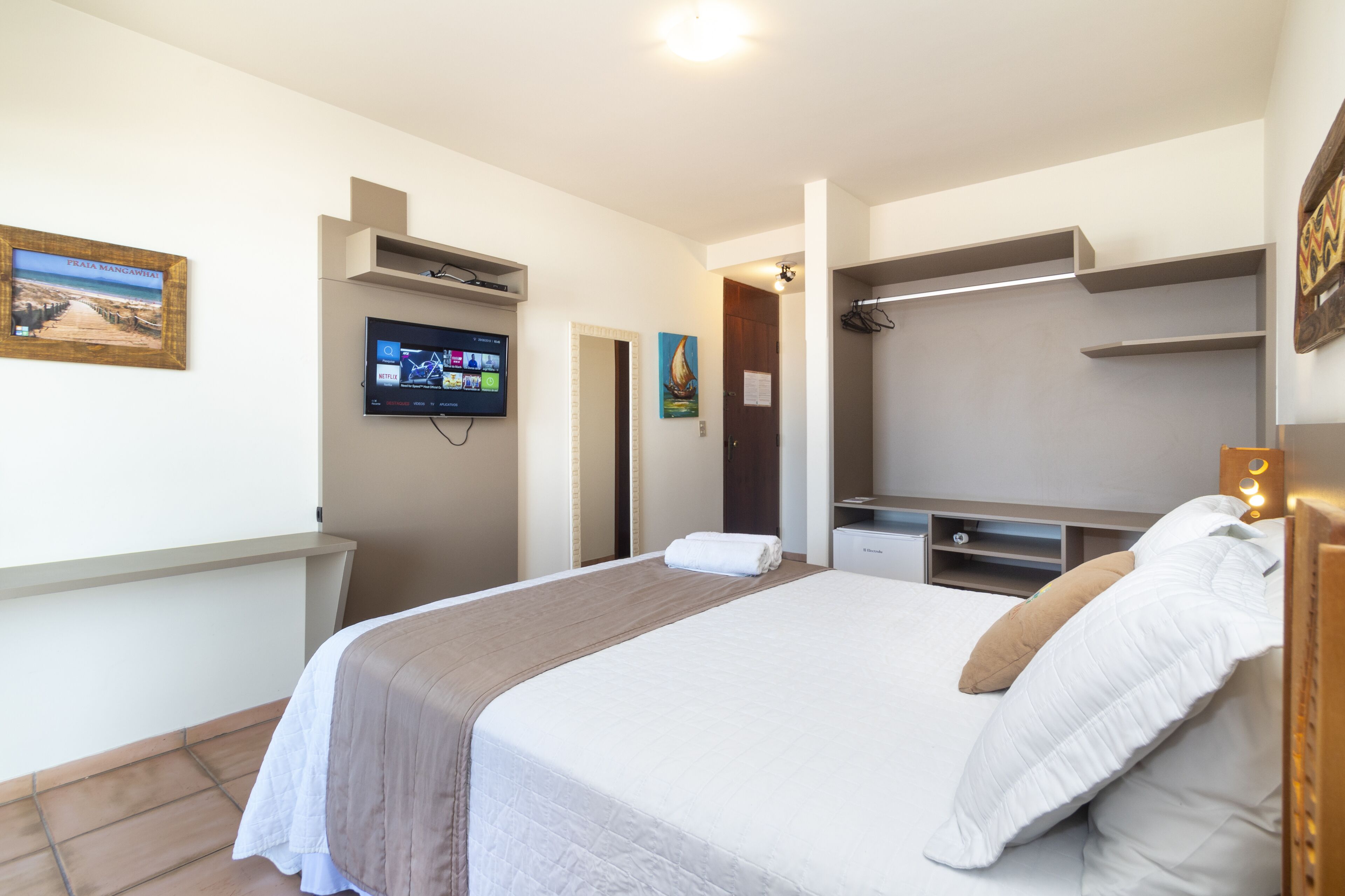 Quarto de hotel com cama, televisão, quadro e porta.
