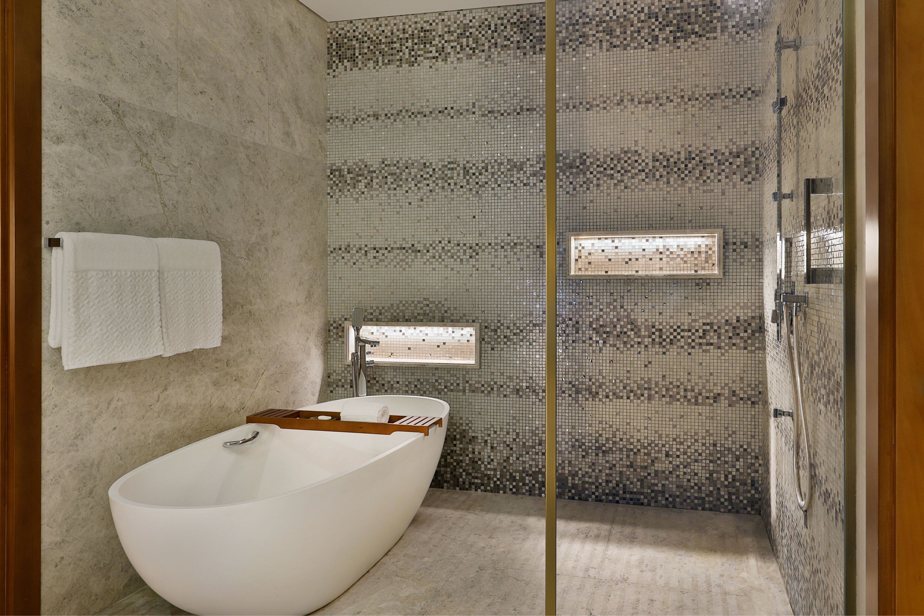 Een moderne badkamer met een vrijstaand bad, een douchegedeelte en een betegelde spatwand.