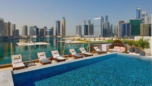 Una piscina infinita en la azotea con sillones de descanso, vista del horizonte urbano y un cuerpo de agua tranquilo.
