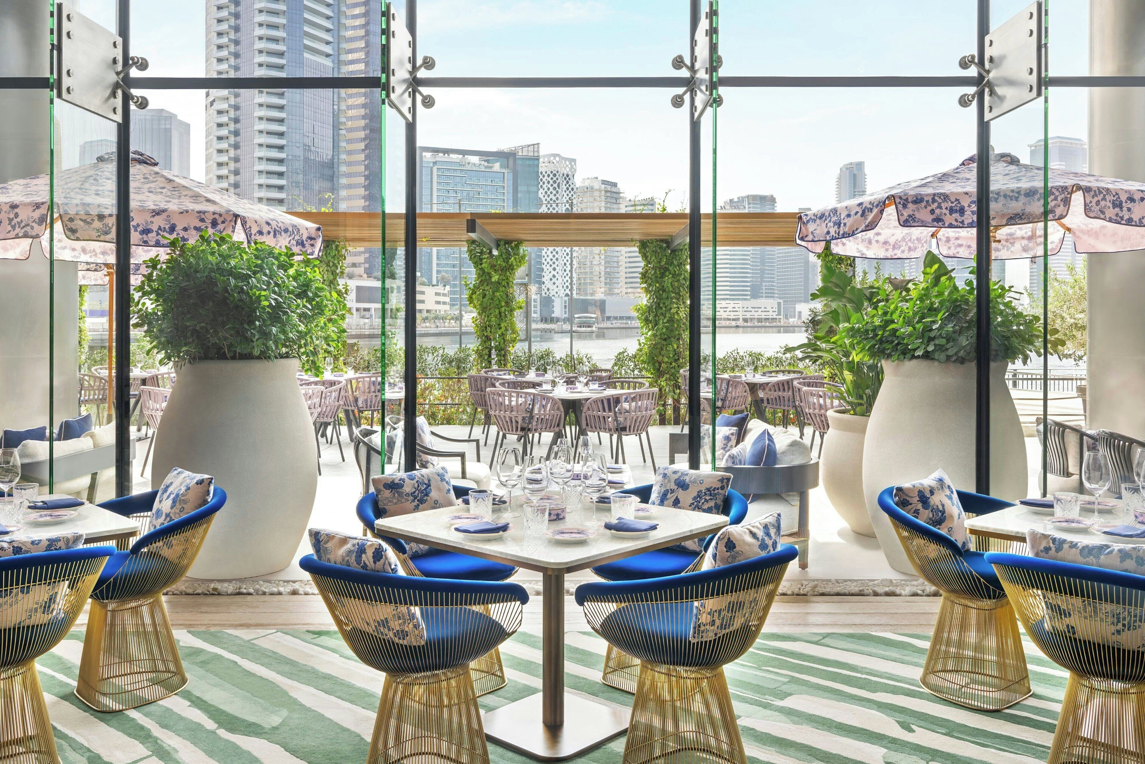 A rooftop dining area with tables and chairs, potted plants, and a view of the city skyline.