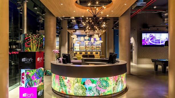 A hotel reception area with a modern design, including a central desk, seating area, and a bar. - Aloft by Marriott Montevideo (Montevideo)