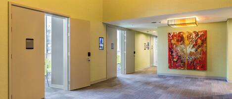 A hotel corridor with a carpeted floor, doors, and a large abstract painting on the wall.