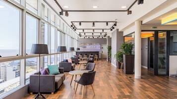 A modern lounge area with seating, a bar, and large windows offering a city view.