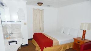 Een hotelkamer met een bed, een nachtkastje met een lamp, een badkamer met een wastafel en een douchegordijn.