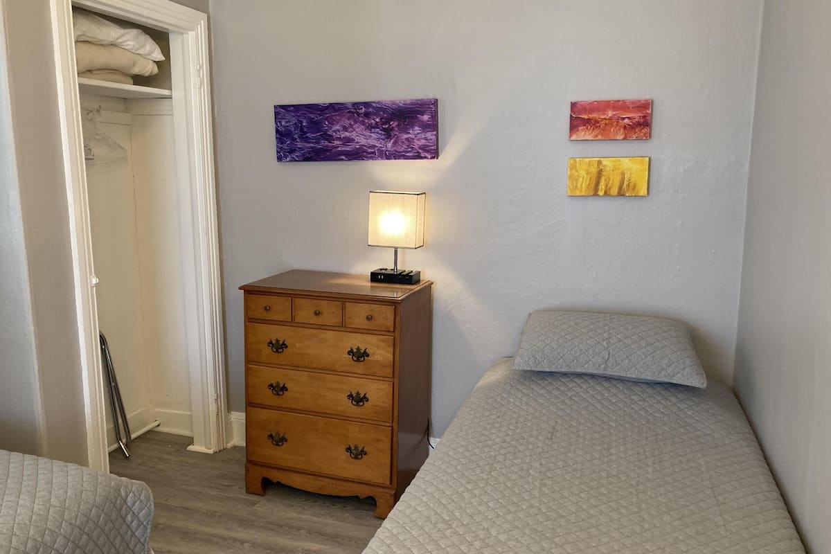 A bedroom with a bed, a wooden dresser, and two wall-mounted paintings.