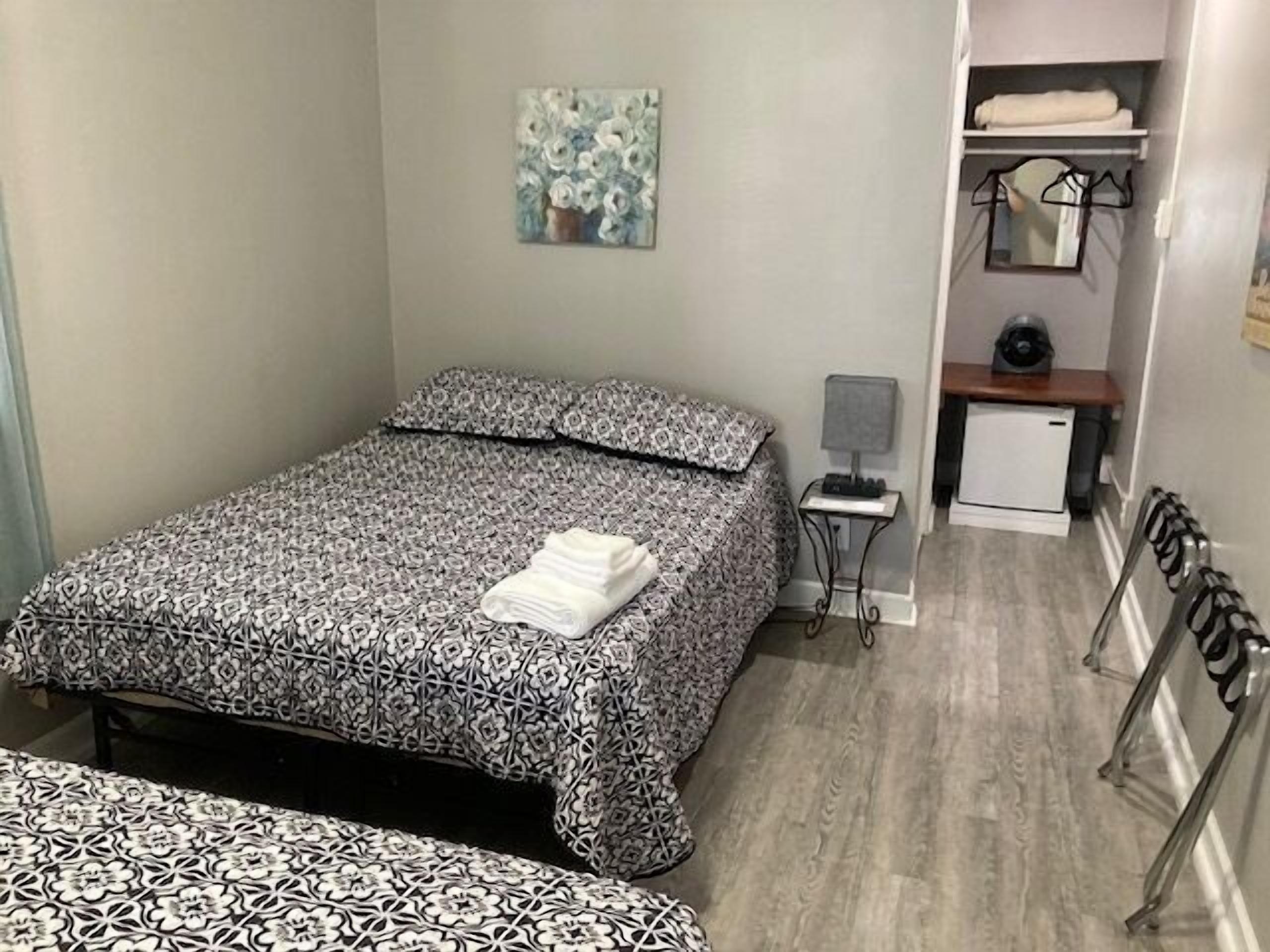 Quarto com cama, escrivaninha pequena, cadeira, radiador e um quadro na parede.
