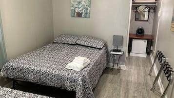 Quarto com cama, escrivaninha pequena, cadeira, radiador e um quadro na parede.
