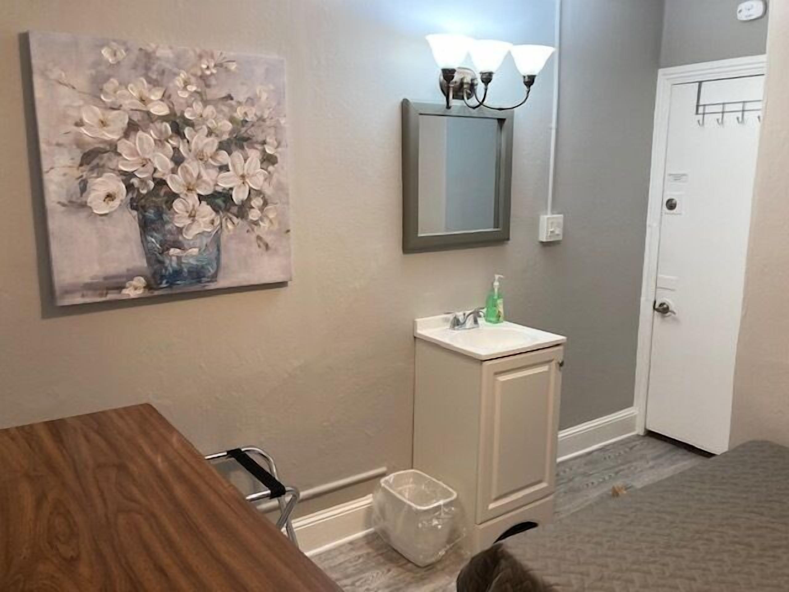 A bathroom with a sink, mirror, and a painting of flowers on the wall.