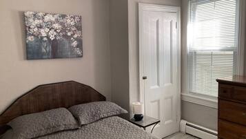 Un dormitorio con cama, cómoda, puerta y ventana con persianas.