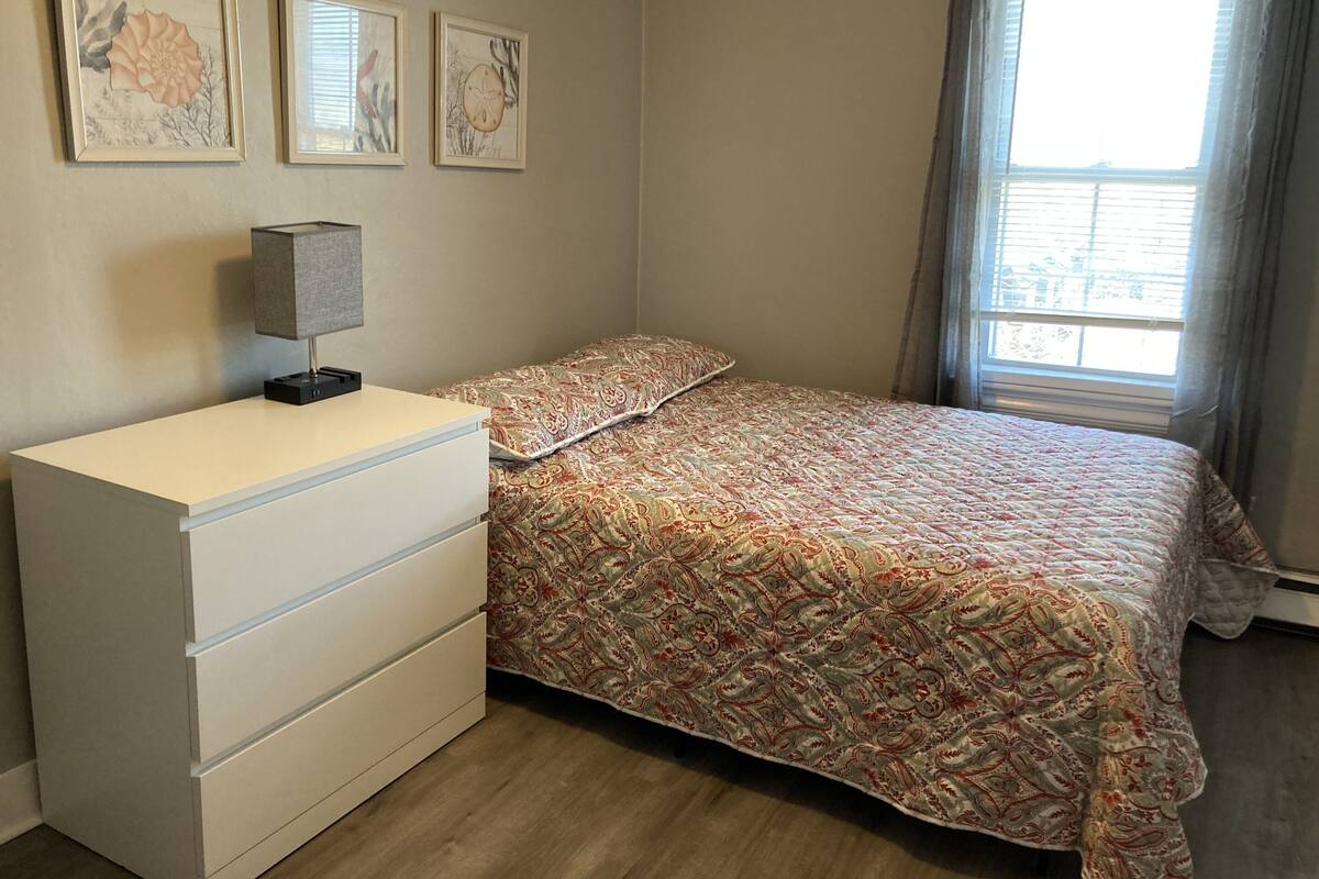 A bedroom with a bed, a dresser, and three framed artworks on the wall.