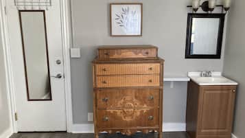 A wooden dresser with drawers and a mirror above it, a small sink, and a door with a coat rack.