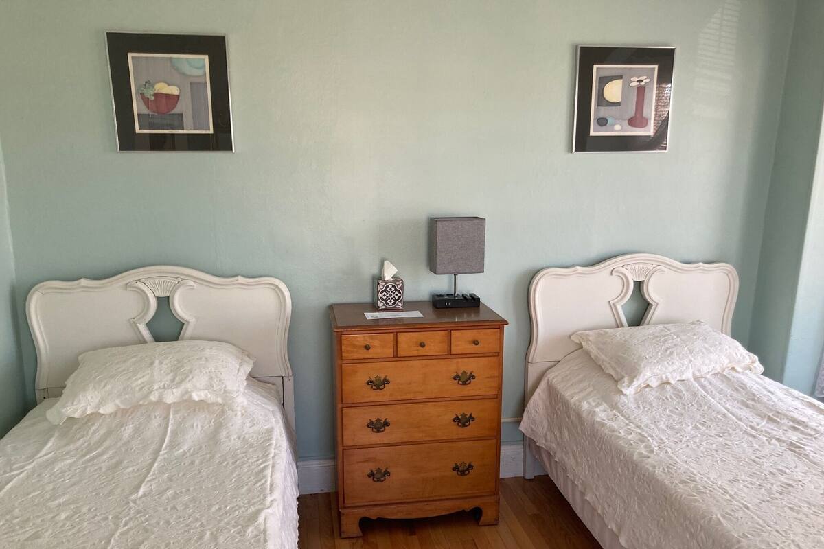 A bedroom with two single beds, a wooden dresser, and two framed pictures on the wall.