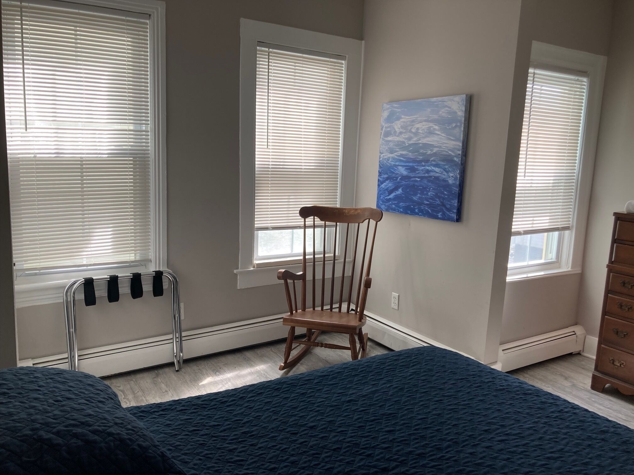Une chambre avec deux lits, un fauteuil à bascule et un tableau au mur.