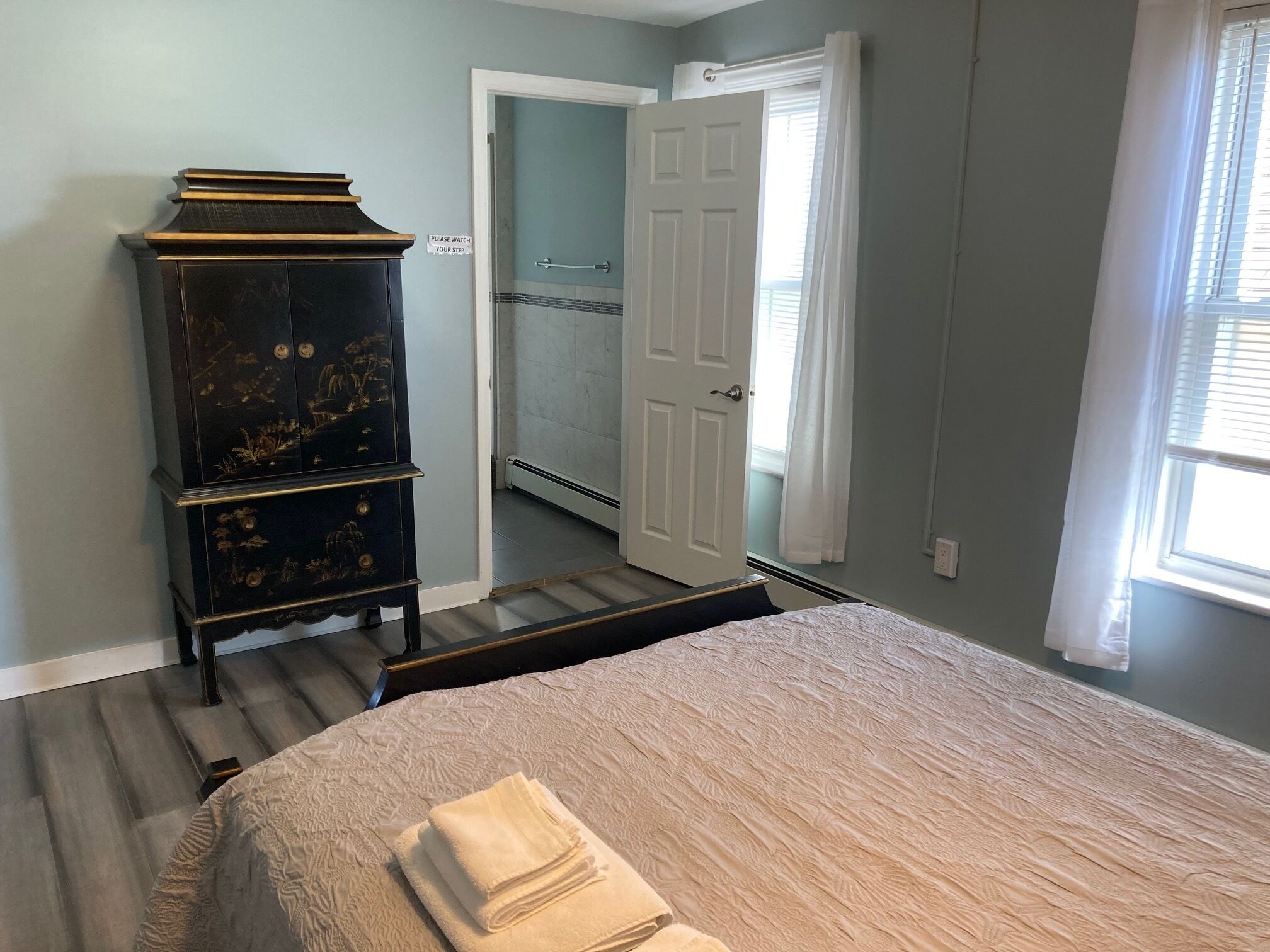 A bedroom with a bed, a dresser, a door leading to a bathroom, and a window.