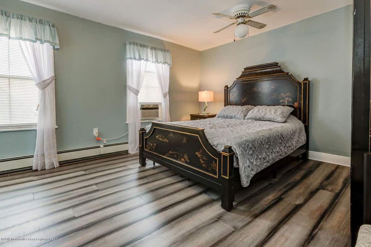 A bedroom with a dark wooden bed, a ceiling fan, and a window with white curtains.