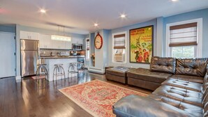 A modern kitchen with stainless steel appliances, a dining area with bar stools, a large brown leather sofa, and a vintage poster on the wall. - Ocean Park Inn (Ocean Grove)