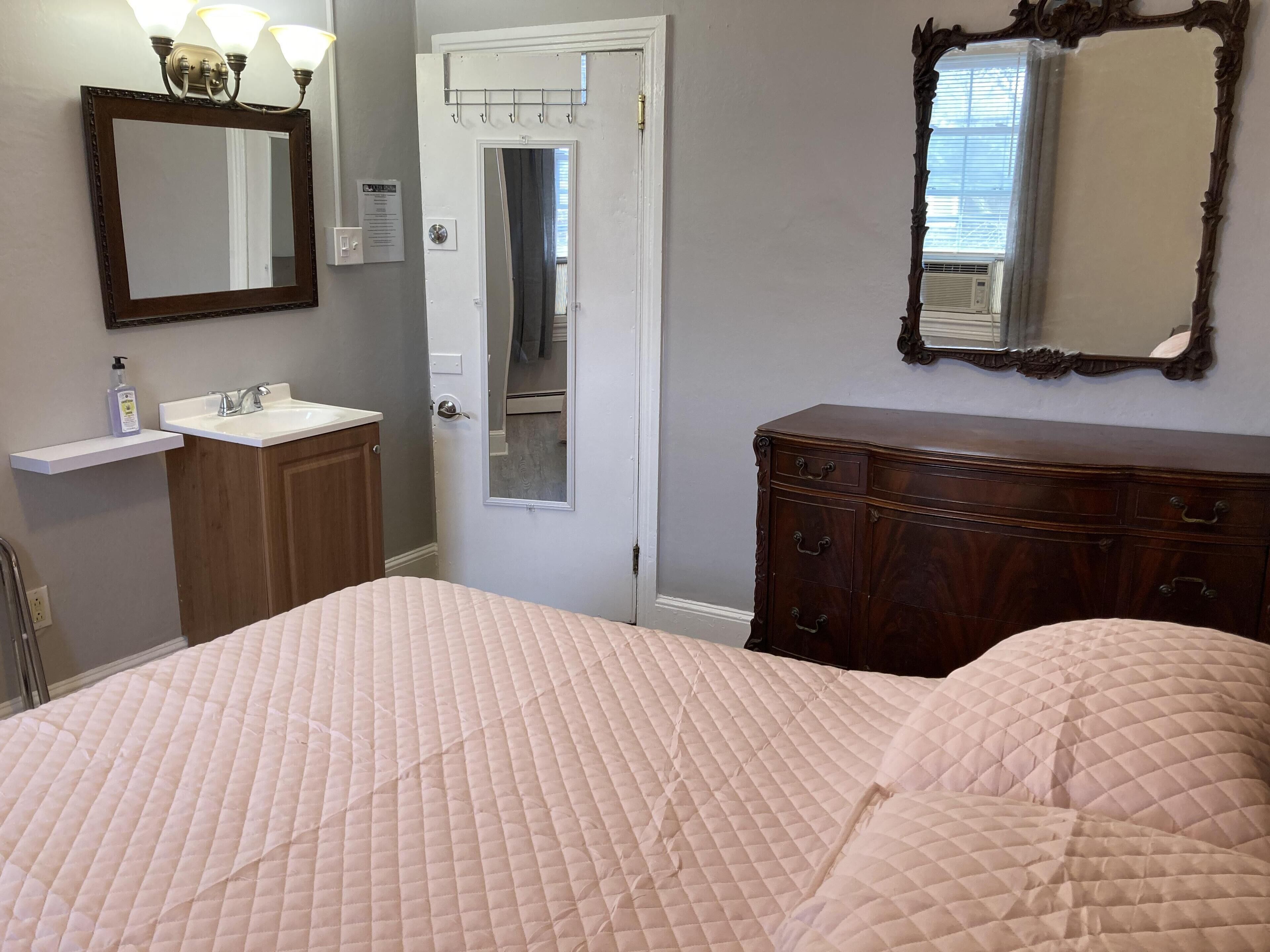 A bedroom with a bed, a dresser, a vanity with a mirror, and a door leading to a bathroom.