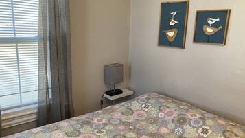 A bedroom with a patterned bedspread, a bedside lamp, and two wall-mounted bird art pieces.