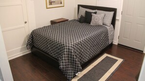 A bedroom with a bed, a nightstand, a framed picture on the wall, and a door. - Summer Leaf (Reseda)