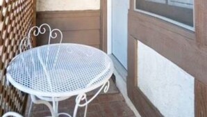 A covered outdoor area with a white metal table and chairs, a wooden lattice fence, and a garage door. - Summer Leaf (Reseda)