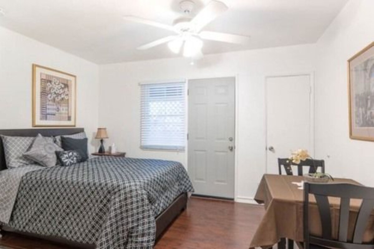 A bedroom with a bed, a ceiling fan, a window with blinds, and a door.
