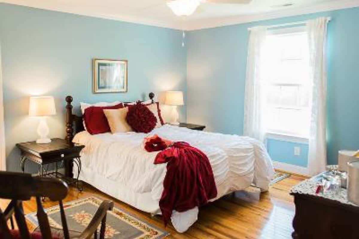 A bedroom with a bed, two bedside tables with lamps, a ceiling fan, a window with curtains, and a framed picture on the wall.