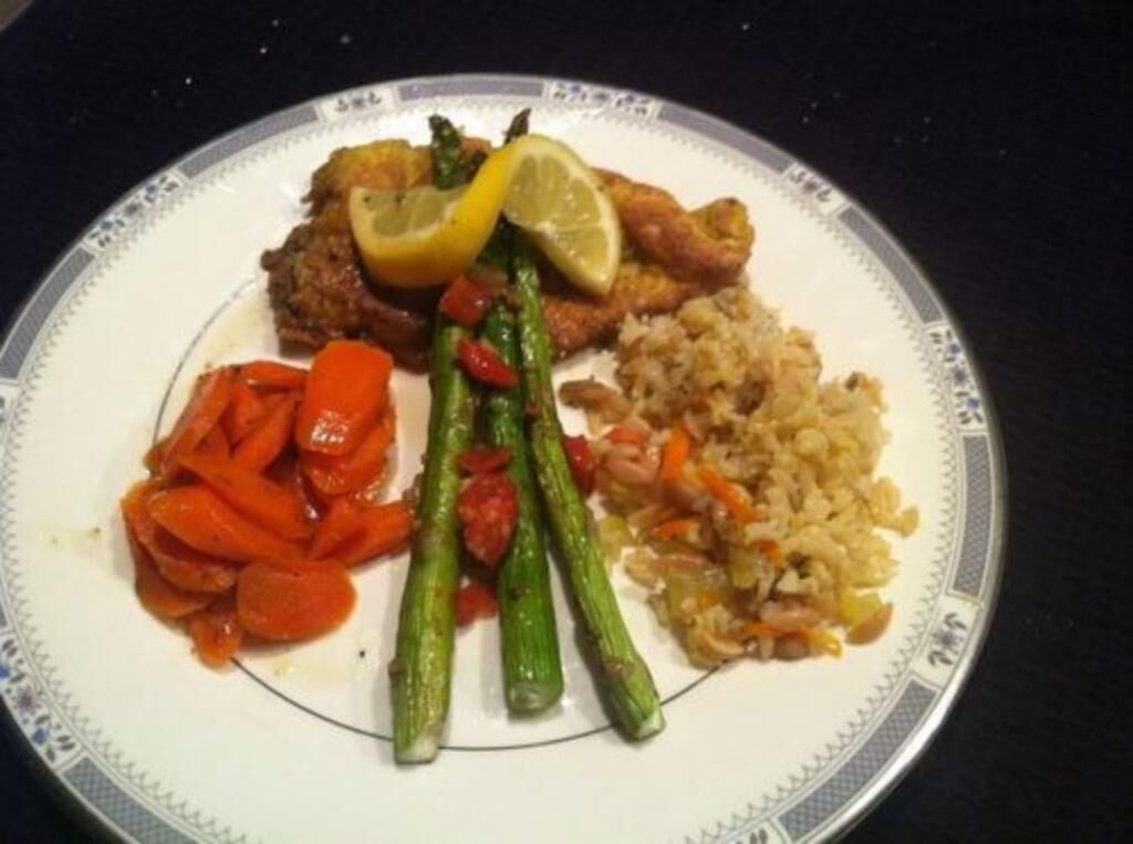 A plate with a variety of food including a piece of meat, rice, carrots, and asparagus.
