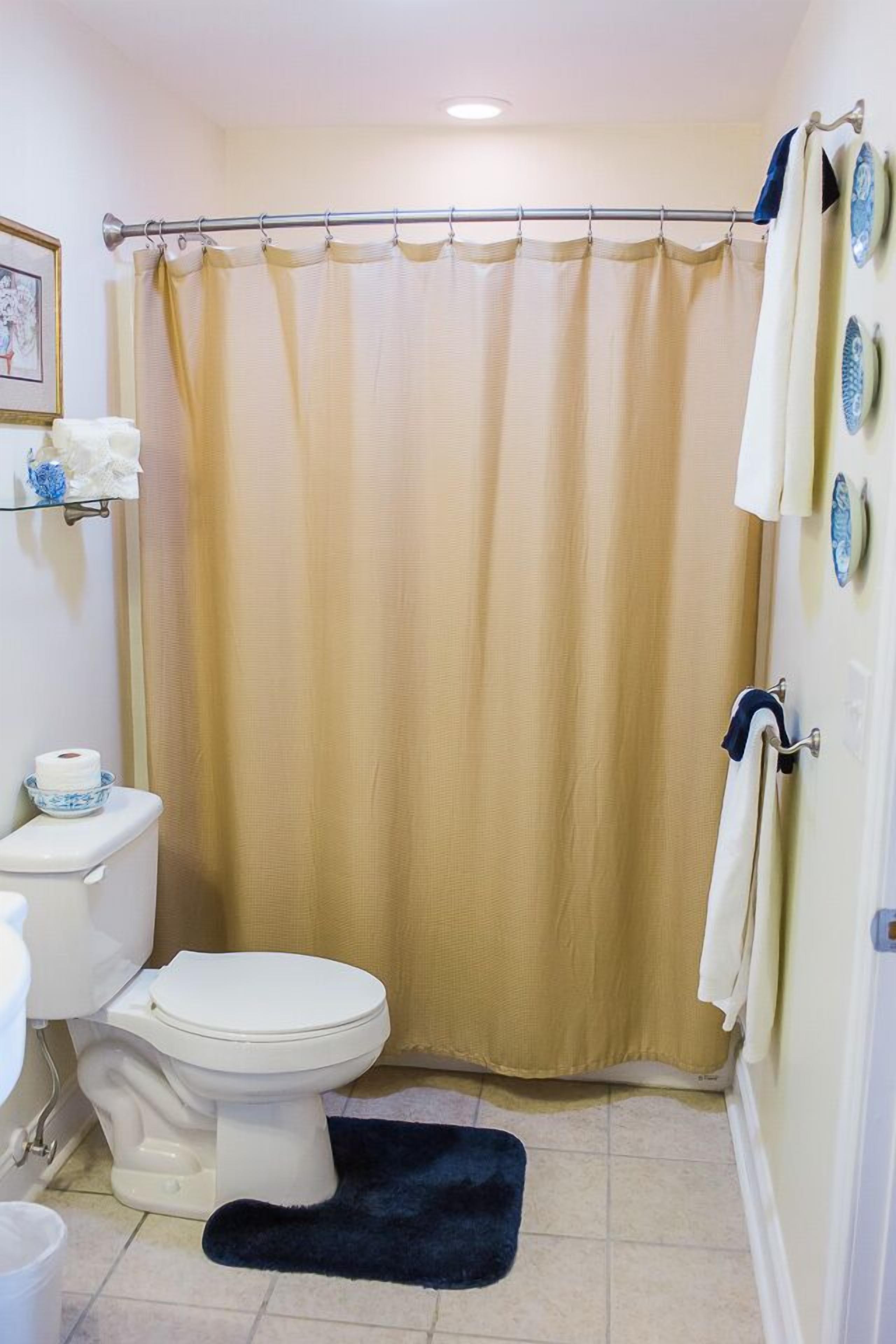 Un baño con inodoro, cortina de ducha color beige y una alfombra de baño azul oscuro.
