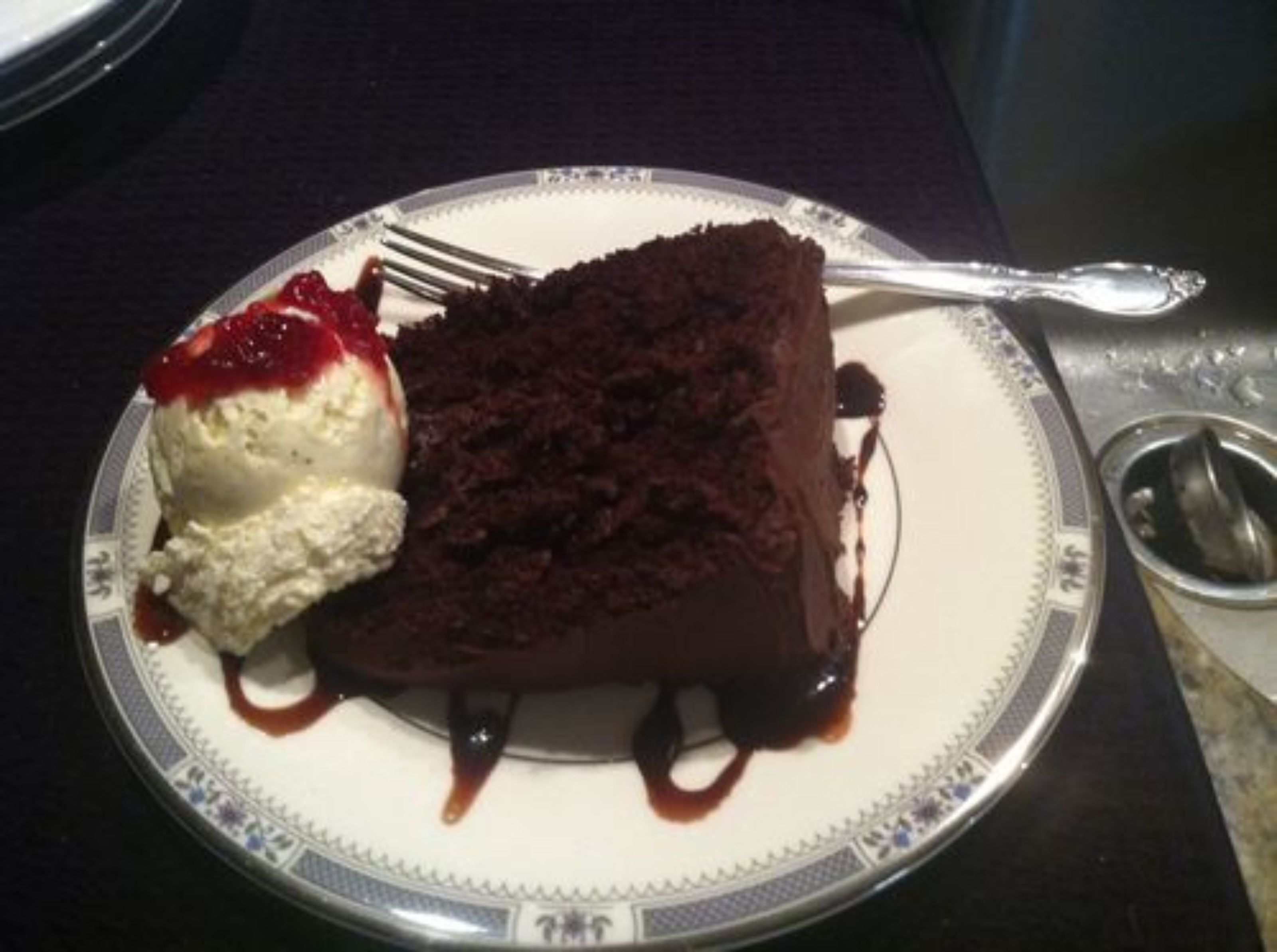 Een bord met een stuk chocoladecake en een bolletje vanille-ijs, alles op een wit bord met een decoratieve rand.