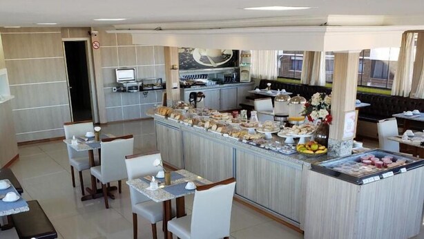 A modern hotel dining area with a central buffet bar, multiple seating arrangements, and a kitchen in the background. - Capão da Canoa - Hotel Rediadri (Capao da Canoa)