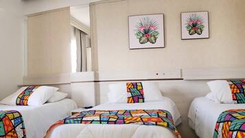 A hotel room with three beds, each with a colorful geometric-patterned bedspread. There are two framed floral paintings on the wall above the beds.